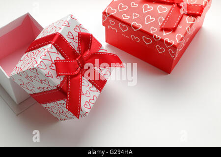 Due decorativo scatole regalo con nastro rosso e cuori stampato vicino. Vista superiore sinistra. Bianco sfondo isolato. Foto Stock