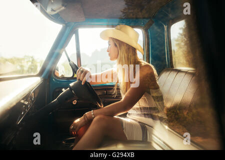 Ritratto di giovane donna seduta sul sedile di guida di una vettura e guardando lontano. Ragazza indossando hat su un viaggio su strada. Foto Stock