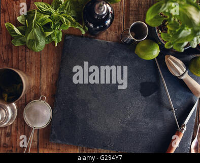 Set di accessori bar e gli ingredienti per la realizzazione di un cocktail disposti su una tavola di legno con copia spazio su scheda nero Foto Stock