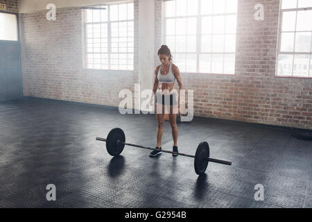 A piena lunghezza Ritratto di muscolare di giovane donna in piedi in palestra con barbells sul pavimento. Forte crossfit femmina alla palestra. Foto Stock