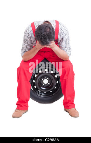 Ha sottolineato il meccanico appoggiato la testa nelle mani e seduto su un pneumatico Foto Stock