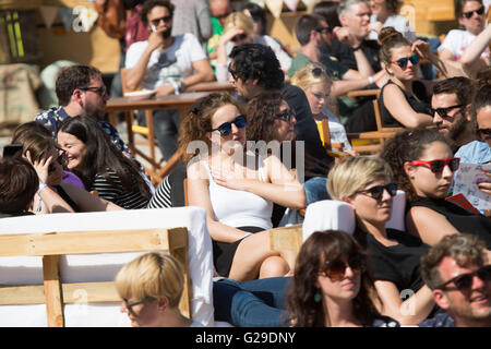 I partecipanti si siedono all'aperto al sole guardando i discorsi dalla Roots Room principale su un grande schermo esterno all'OFFF Barcelona presso il Disseny Hub Museum of Design di Barcellona, Spagna, 26 maggio 2016. Il primo giorno del festival OFFF (Let's Feed the Future) a Barcellona. Questo festival del design è giunto al suo 16° anno. Nella foto: Una folla si riunisce all'esterno per guardare le presentazioni su un grande schermo. Crediti: Rob Watkins/Alamy Live News Foto Stock