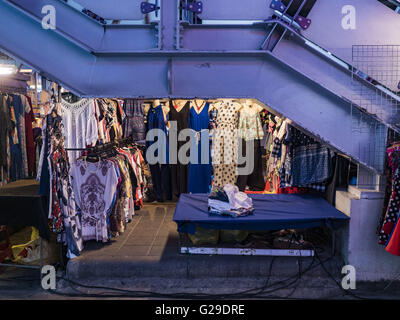 Bangkok, Bangkok, Thailandia. 26 Maggio, 2016. Un negozio di abbigliamento sotto le scale che portano al BTS Sala Daeng stazione dello skytrain in Silom Road mercato notturno. Il mercato notturno in Silom Road, vicino a Bangkok il famoso di Patpong area turistica, viene chiuso da Bangkok di governo municipale. I fornitori sono stati avvisati del fatto che dovranno lasciare il marciapiede sulla Silom Road per la fine di maggio 2016. Il mercato è l'ultima strada del mercato di essere arrestato da funzionari della città come parte del programma del governo per pulire fino a Bangkok. La Via Silom night market vende principalmente orientato turistica vestiti, poco costoso arte Tailandese, Foto Stock