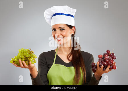 Donna cook holding grappolo di uva e sorridente Foto Stock
