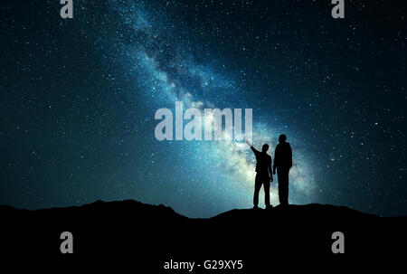 La Via Lattea con la silhouette di una famiglia. Padre e figlio che puntare il dito nella notte cielo stellato sulla montagna. Paesaggio notturno Foto Stock