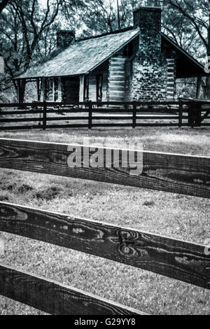Concettuale vista artistica attraverso le stecche di una staccionata in legno di un palazzo del XIX secolo in stile rustico stile log cabin con portico antistante ed erba Foto Stock