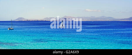 Barche a vela in acque turchesi, costa nord di Fuerteventura in background, Punta Papagayo, Playa Blanca, Lanzarote Foto Stock