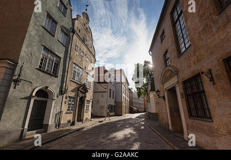 Un viandante attraversa la strada in sera la luce del sole, nella parte anteriore dei tre fratelli, su Mazā Pils iela, Riga, Lettonia. Foto Stock