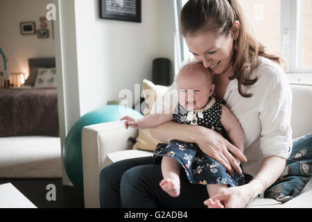 Madre seduto sul divano con il bimbo che piange la figlia (2-5 mesi) in soggiorno Foto Stock
