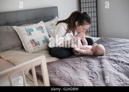 Madre kissing baby di mia figlia (2-5 mese) piedi in camera da letto Foto Stock