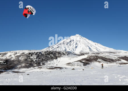 Snowkiting o kiteboarding - sportivo scivola su sci sulla neve su uno sfondo di attivo vulcano Koryaksky (penisola di Kamchatka). Foto Stock