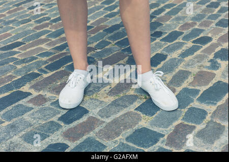 Le gambe e i piedi di una giovane donna in piedi su un acciottolato stret Foto Stock