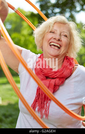Felice donna senior facendo sport con cerchio in un giardino estivo Foto Stock