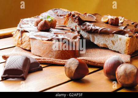 Due fette di pane con crema di cioccolato e nocciole su una tavola di legno.sfondo marrone. Nocciola e Cioccolato decorazione. Foto Stock