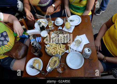 Rio de Janeiro lifestyle - persone godere il tempo libero al tavolo sul marciapiede in un tipico bar di Rio ( chiamato barzinho ) - avente chope ( birra alla spina o birra, birra servita da una botte o barile ) e antipasti - filetto con cipolla, patatine fritte e farofa, tostati, farina di manioca miscela con il burro, il sale, olive, cipolla, aglio, uova sode, e/o di pancetta. Foto Stock