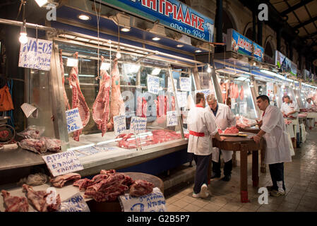 Macelleria Carne Fresca Mercato Dimotiki Agora Atene Grecia | ATENE, Grecia — Macellai in camici bianchi preparano tagli di agnello e manzo sotto carcasse appese al Dimotiki Agora, noto anche come Varvakios Agora, il più grande mercato al dettaglio di prodotti freschi del centro di Atene. Insegne scritte a mano indicano il prezzo dell'agnello e del vitello di Naxos al chilo su bancarelle che operano all'interno del mercato coperto sin dalla sua completazione da parte del Comune di Atene nel 1886. Foto Stock