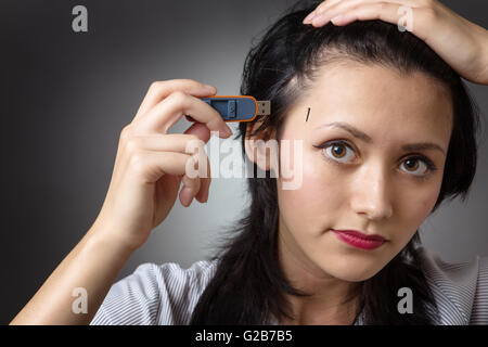 Close-up colpo di testa di un business donna tenendo un memory stick per collegarlo al lato della sua testa, shot su un backgro grigio Foto Stock