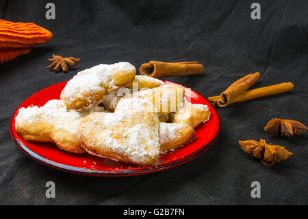 Biscotti fatti in casa nella polvere di zucchero con un tovagliolo arancio, bastoncini di cannella e anice stellato su un tessuto nero lo sfondo Foto Stock