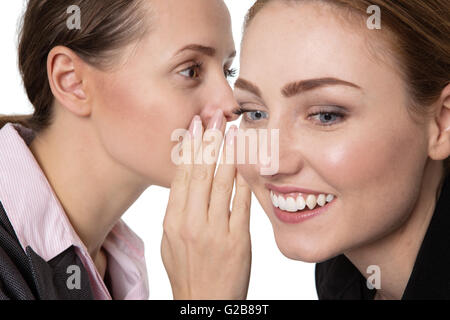 Immagine ravvicinata di due felici, piuttosto le donne d'affari, la condivisione di una chiave segreta e sussurra in ogni altro orecchio. Foto Stock