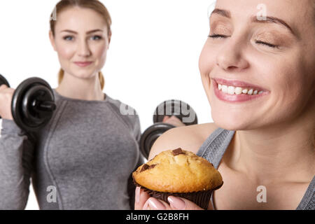 Due donne sportive azienda muffin e manubri su sfondo bianco Foto Stock