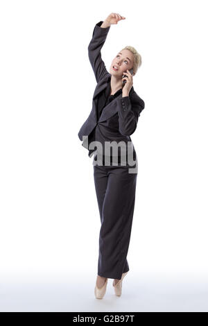 Studio shot di una bella bionda modello di business, indossa una tuta e scarpe da ballo, è enpointe mentre tiene un telefono cellulare, isola Foto Stock