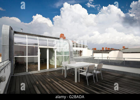 Conversione di Dach o soppalco in Reichenberger Strasse, Kreuzberg. Legno moderno decking contemporanea con tavolo da pranzo e sedie. Vetro le porte del patio. Curvato finestre da pavimento a soffitto. Foto Stock