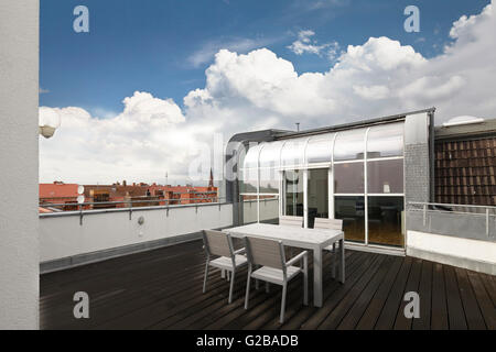 Conversione di Dach o soppalco in Reichenberger Strasse, Kreuzberg. Legno decking al di fuori del loft con tavolo da pranzo e sedie. Patio in vetro porte e finestre da pavimento a soffitto. Foto Stock