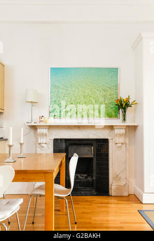 Pembridge Square, Notting Hill. Vista di una pittura moderna al di sopra di un camino. Vista parziale di un legno tavolo da pranzo con sedie bianche. Pavimenti in legno. Foto Stock