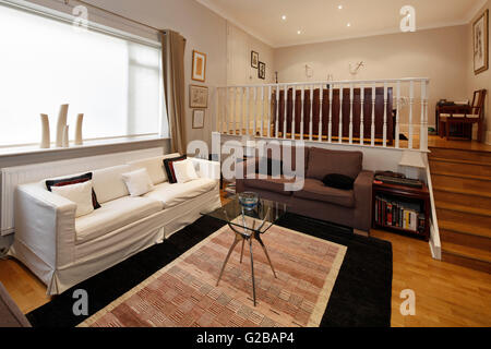 Walden House, Marylebone High Street. Vista di un livello due soggiorno. Scala con ringhiera in bianco. Arredamento contemporaneo con ampia finestra. Foto Stock