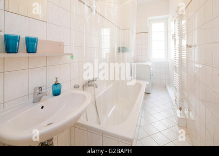 Wisbyer Strasse 59. Una moderna stanza da bagno con piastrelle bianche e caratteristiche di bianco. Accessori blu. Foto Stock