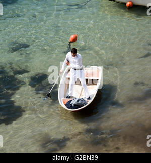 DUBROVNIK Croazia un uomo vestito di bianco pantaloni e camicia usando una racchetta per spostare il suo dinghy in tutta la Città Vecchia porto Foto Stock