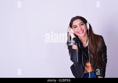 La musica. Giovane donna ispanica l'ascolto di musica con le cuffie. Giocoso donna sorridente isolate su uno sfondo grigio. Foto Stock