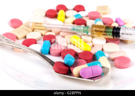 Pillole colorate con cucchiaio d'argento sul tavolo bianco Foto Stock