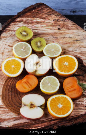 Fette di vari frutti sul taglio fresco di un moncone di legno. Kiwi, arancio, Apple, limone e persimmon Foto Stock