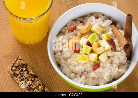 Porridge di fiocchi d'avena con mele, cannella, dadi e goji bacche. Barre di muesli, frutta fresca e succhi di arancia su sfondo di legno Foto Stock