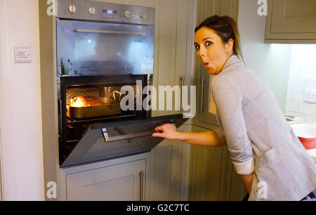Giovane donna La cottura arrosto di agnello nella sua nuova cucina con doppio forno elettrico Foto Stock