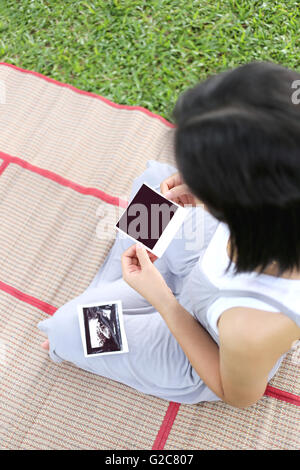 Asian Le donne in stato di gravidanza mostrano film di ultrasuoni baby picture sul suo ventre in mano a giardino. Foto Stock