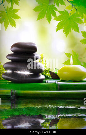 Impilati pietre nere e candela in bambù. Riflesso in acqua in natura. Concetto di calma e relax. Trattamenti alternativi, Foto Stock