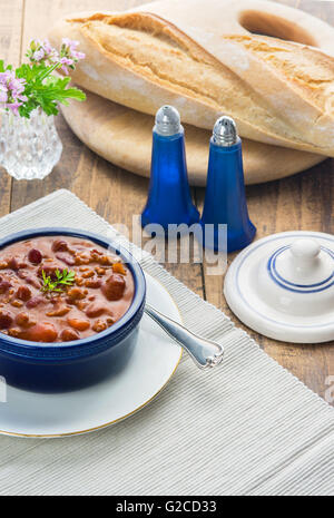 L'immagine verticale di una tabella che mostra un pasto di chili con la canna da zucchero su una tavola di legno insieme con il pane in una finestra luminosa luce. Foto Stock