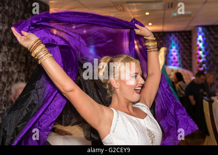 Bionda donna inglese eseguendo una danza di Bollywood con un viola e mantello nero in un ristorante indiano a Warrington, Inghilterra Foto Stock