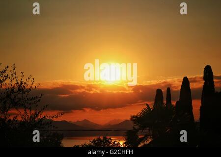 Un bel colore arancione tramonto su un lago con alberi in middleground. Foto Stock