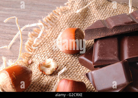 Cumulo di porzioni artigianale cioccolato sulla tela sacco con le nocciole su un marrone tavolo in legno con decorazione di paglia. Posizione orizzontale Foto Stock