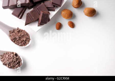 Porzioni e scaglie di cioccolato con mandorle su una porcellana bianca contenitore su un bianco tavolo in legno isolato. Posizione orizzontale Foto Stock