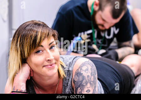 BELFAST, IRLANDA DEL NORD. 28 MAGGIO 2016 - 6th Conferenza del Tattoo dell'Irlanda del Nord. Una cliente femmina sorride mentre ha un tatuaggio sul polpaccio della gamba Foto Stock