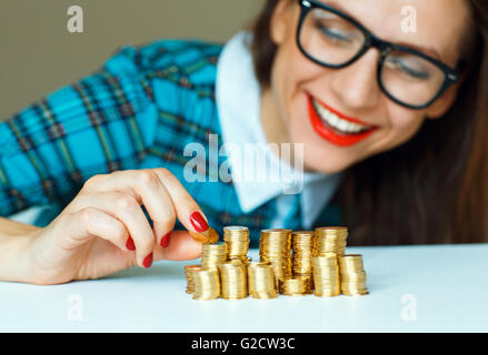 Salvataggio, donna sorridente di impilamento delle monete in oro in colonne Foto Stock