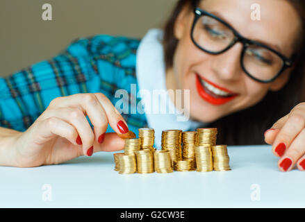 Salvataggio, donna sorridente di impilamento delle monete in oro in colonne Foto Stock