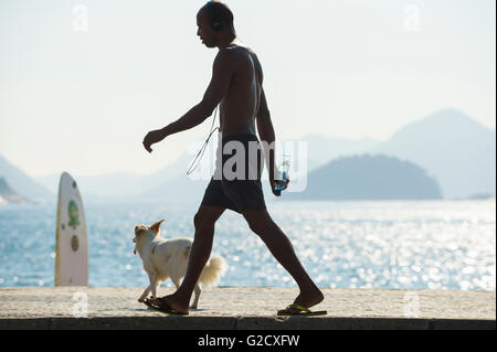 RIO DE JANEIRO - Aprile 3, 2016: un giovane brasiliano uomo cammina con un cane lungo un mattino luminoso vista del lungomare di Copacabana. Foto Stock