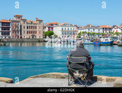 Pescatore pesca in Saint Jean de Luz - Ciboure porto di pesca con maison de Le Infante Joanoenia in background. La Francia. Foto Stock