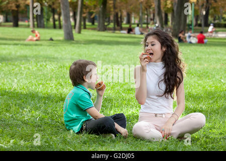 Kid boy e la donna di mangiare un muffin nel parco seduto sull'erba nel parco Foto Stock