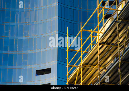 Scaffolding on a building site with a multi story glass tower building in the background Foto Stock